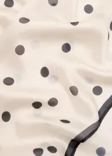 Pañuelo cuadrado de tejido satinado color crudo con estampado de lunares negros y borde oscuro.