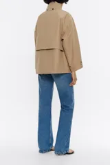 Chaqueta tipo gabardina corta de tejido técnico con corte en línea A, cuello alto con capucha plegable, cierre frontal con cremallera y mangas anchas con trabillas en los puños.