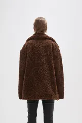 Campera de textura tipo corderito en color marrón, con cuello solapa y cierre frontal mediante tres botones tipo duffle con presillas de cuero sintético.