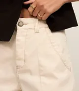 Short de mujer de sarga color beige claro, tiro alto, con pespunte contrastante en color blanco o crema. Presenta un corte regular y bolsillos delanteros y traseros.