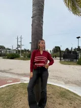 Sweater de punto color bordó con cuello polo y escote en V, de manga larga. Presenta un diseño con rayas horizontales en color crema en la parte inferior.