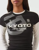 Top de manga larga con diseño superpuesto, que combina una remera de manga corta negra con estampado gráfico frontal y mangas largas blancas debajo. Presenta un ajuste al cuerpo y estilo deportivo.
