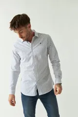 Camisa de hombre de corte slim fit, confeccionada en algodón con diseño de rayas verticales finas en color azul sobre fondo blanco. Presenta cuello clásico, cierre frontal con botones y logo bordado en el pecho.