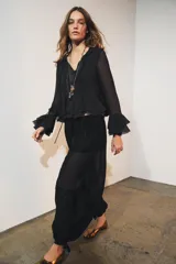 Camisa de viscosa con cuello redondo y escote en pico ajustable mediante lazadas. Presenta cierre frontal con botones, mangas largas con terminación evasé y detalle de volantes en el mismo tejido.