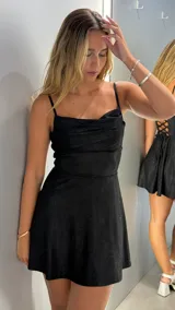 Vestido corto negro con brillo, escote drapeado tipo *cowl neck* y tirantes finos. La falda es acampanada y el vestido tiene un ajuste ceñido en el torso.