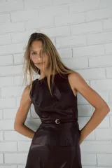 Top sin mangas de efecto piel en color negro, con cuello redondo, corte entallado y bajo evasé. Incluye un cinturón fino integrado y cierre de cremallera oculta en la espalda.
