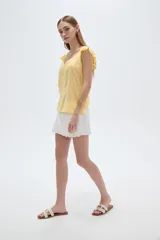 Musculosa amarilla de viscosa, con cuello en V y breteles anchos decorados con volados. Presenta un corte holgado.