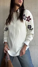 Sweater de punto color natural con cuello redondo y diseño de flores bordadas en las mangas. Presenta puños y ruedo acanalados.