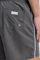 Short de baño oversize gris, con cintura elástica ajustable mediante cordón, bolsillos laterales y detalle de cinta estampada en los laterales.