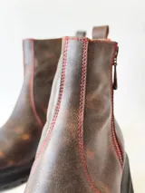 Botas cortas de cuero color chocolate, con elástico lateral, cierre interno con cremallera roja, pespuntes rojos y suela track.