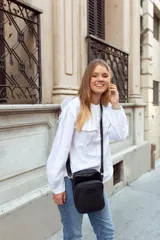 Bandolera negra de cuero con correa ajustable, cierre superior y bolsillo externo con cierre. Incluye bolsillo interno y logo de la marca grabado en el frente.