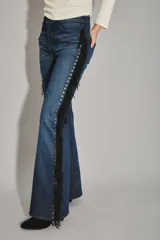 Jean de corte recto y tiro medio, color azul oscuro, con detalle de flecos negros y ojales metálicos a lo largo de la costura lateral.