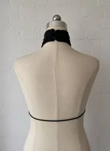 Top negro de estilo halter con cuello alto y abertura frontal profunda, ajustado mediante lazos. Confeccionado en tela semitransparente y ligera.