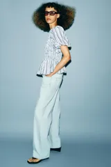 Top de cuello redondo con cuerpo de nido de abeja elástico y mangas cortas abullonadas con elástico en los puños. Presenta un diseño de rayas verticales en tonos azul, rojo y negro, con un bajo estilo peplum y cierre de botón en la espalda.