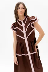 Vestido midi de lino blanco con diseño de broderie, cuello alto, cierre frontal con botones y volados decorativos en los hombros y el cuerpo.