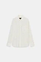 Camisa fluida de corte oversize confeccionada en mezcla de viscosa, con diseño de rayas verticales finas en tono beige sobre fondo blanco. Presenta cuello solapa, cierre frontal con botones, manga larga con puños y un bolsillo de plastrón en el pecho.