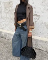 Cinturón trenzado de cuero negro con hebilla metálica circular grande de estilo western.