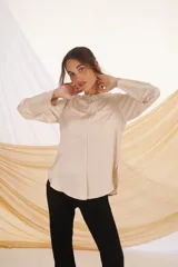 Camisa verde esmeralda de corte recto, cuello mao, cierre frontal con botones y mangas largas con puños abotonados. Presenta dos bolsillos de parche en el pecho.