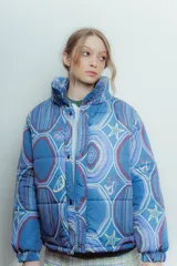 Campera puffer de diseño capitoneado, confeccionada en tela impermeable con estampado multicolor de motivos marinos y cadenas. Presenta cuello alto, cierre frontal con botones a presión y puños elásticos.