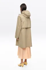 Gabardina de largo medio color beige, corte recto, con capucha ajustable, cierre frontal de cremallera y botones a presión, bolsillos laterales y mangas largas.