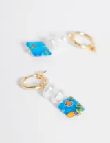 Par de aros dorados tipo argolla con dije colgante compuesto por dos perlas sintéticas y una pieza de vidrio cuadrada con diseño floral.