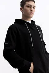 Canguro con capucha y cordones ajustables, de corte holgado y bolsillo frontal tipo canguro. Presenta un pequeño logo estampado en el pecho.