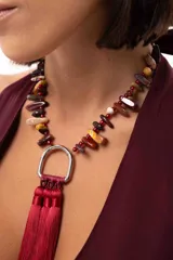 Collar corto con cadena de piedras naturales en tonos tierra y un dije central metálico en forma de herradura del que cuelgan tres borlas de seda en color bordó.
