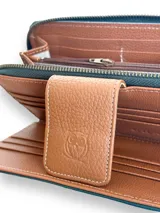 Billetera tipo sobre confeccionada en cuero vacuno color verde con textura tipo cocodrilo. Tiene cierre perimetral con cremallera, correa de mano desmontable y broche de cuero marrón con logo de la marca.