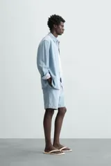 Shorts de denim de algodón, color celeste lavado, de corte regular fit y largo hasta la rodilla. Presenta cierre frontal con cremallera y botón, bolsillos delanteros y bolsillos traseros de plastrón. El borde inferior tiene un acabado deshilachado.