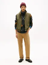 Chaleco verde militar Tommy Hilfiger de cuello alto, con cierre frontal de cremallera y dos bolsillos laterales de ojal. Presenta un diseño sin mangas con logo monotipo bordado en el pecho.