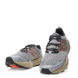 Championes de trail running New Balance modelo Garoe, color gris con detalles en naranja y suela en tono arena. Presentan tecnología Fresh Foam en la entresuela para mayor amortiguación y refuerzos en la puntera para mayor protección.