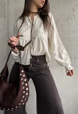 Camisa beige de manga larga, con detalles bordados en el frente y botones decorativos.