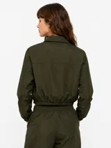 Campera corta de nylon color beige, con cuello camisero, cierre frontal con botones a presión, mangas largas con puños elásticos y cordón ajustable en la cintura.