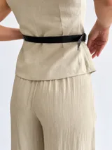 Conjunto de dos piezas para mujer en color beige, compuesto por un chaleco cruzado sin mangas con cinturón lateral y un pantalón de corte amplio.