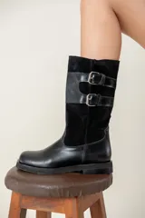 Bota de caña media combinada en cuero liso y gamuza, color negro. Presenta un diseño con doble hebilla lateral metálica y cierre de cremallera vertical en el lateral interno. Cuenta con suela plana y tacón bajo.