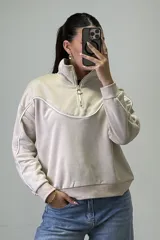 Buzo deportivo color beige con cuello alto y cierre frontal parcial. Presenta costuras decorativas con ribetes blancos en el pecho y a lo largo de las mangas. Posee puños y ruedo elásticos.