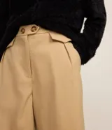 Bermuda de sastrería de corte recto y tiro alto, color beige. Cuenta con detalles de solapas plisadas y cierre con dos botones en la cintura.