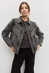 Campera de jean color gris con efecto acid wash, corte clásico y cierre frontal de botones metálicos. Presenta cuello camisero, bolsillos ribeteados y está decorada con apliques de tachas plateadas en el cuello, el canesú frontal, los bordes de la botonera, los bolsillos y el ruedo.