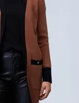 Cardigan largo tejido color marrón con ribetes negros en contraste, bolsillos delanteros y mangas largas.