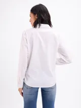 Camisa beige de manga larga con cuello camisero, cierre frontal con botones y diseño de pespuntes y bordados en relieve con formas florales en la parte inferior y lateral.