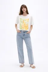 Remera de algodón color blanco, de corte holgado y manga corta, con cuello a la base. Presenta un estampado frontal rectangular en tonos amarillos y verdes con motivos botánicos, realzado con detalles bordados y lentejuelas.