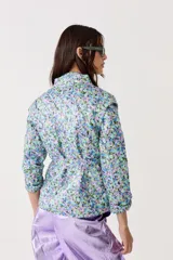 Chaqueta capitoneada con estampado floral y terminación metálica, cuello alto, cierre frontal escondido, cinturón para atar y bolsillos laterales.