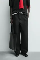 Pantalón de corte balloon fit y estilo relajado, confeccionado en tejido de algodón. Presenta pliegues frontales, cintura con trabillas, cierre frontal con cremallera y botón, bolsillos delanteros y bolsillos traseros de vivo.