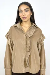 Camisa de pana fina color beige, con volados decorativos en los hombros y a lo largo de la botonadura frontal. Presenta cuello clásico, mangas largas con puños y cierre mediante botones dorados.
