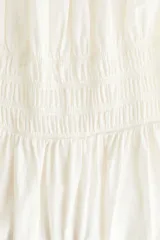 Vestido midi color blanco en tejido liviano, con escote redondo fruncido y abertura en V con tira fina ajustable en el frente. Tiene mangas cortas abullonadas, cintura elástica en punto smock y falda acamponada de corte midi.