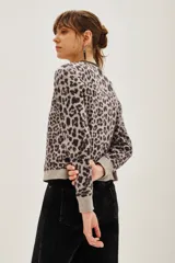Cardigan de punto con estampado animal print en tonos gris y negro. Presenta cuello redondo con detalle de pedrería brillante, cierre frontal con botones y puños acanalados.