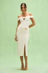 Vestido midi color blanco con escote tipo hombros caídos, detalle de broche decorativo en el centro del pecho y en la cintura, y abertura frontal en la falda.