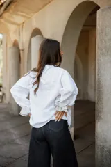 Camisa de lino blanca con cuello camisero, cierre frontal de botones de nácar y mangas largas con puños en contraste de tela rayada.