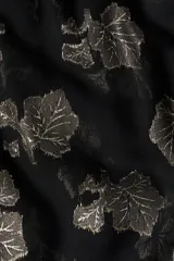 Blusa de corte holgado en tejido jacquard transparente con diseño de hojas metalizadas. Presenta cuello mao con frunces, abertura frontal con tiras finas, ribete de volados y mangas largas tipo globo con puños elásticos.