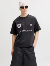 Remera negra de manga corta y cuello redondo, de corte holgado. Cuenta con estampado frontal de estilo deportivo que incluye la inscripción "LA GRACIOSA", un parche circular con diseño de sol y el logo de la marca.